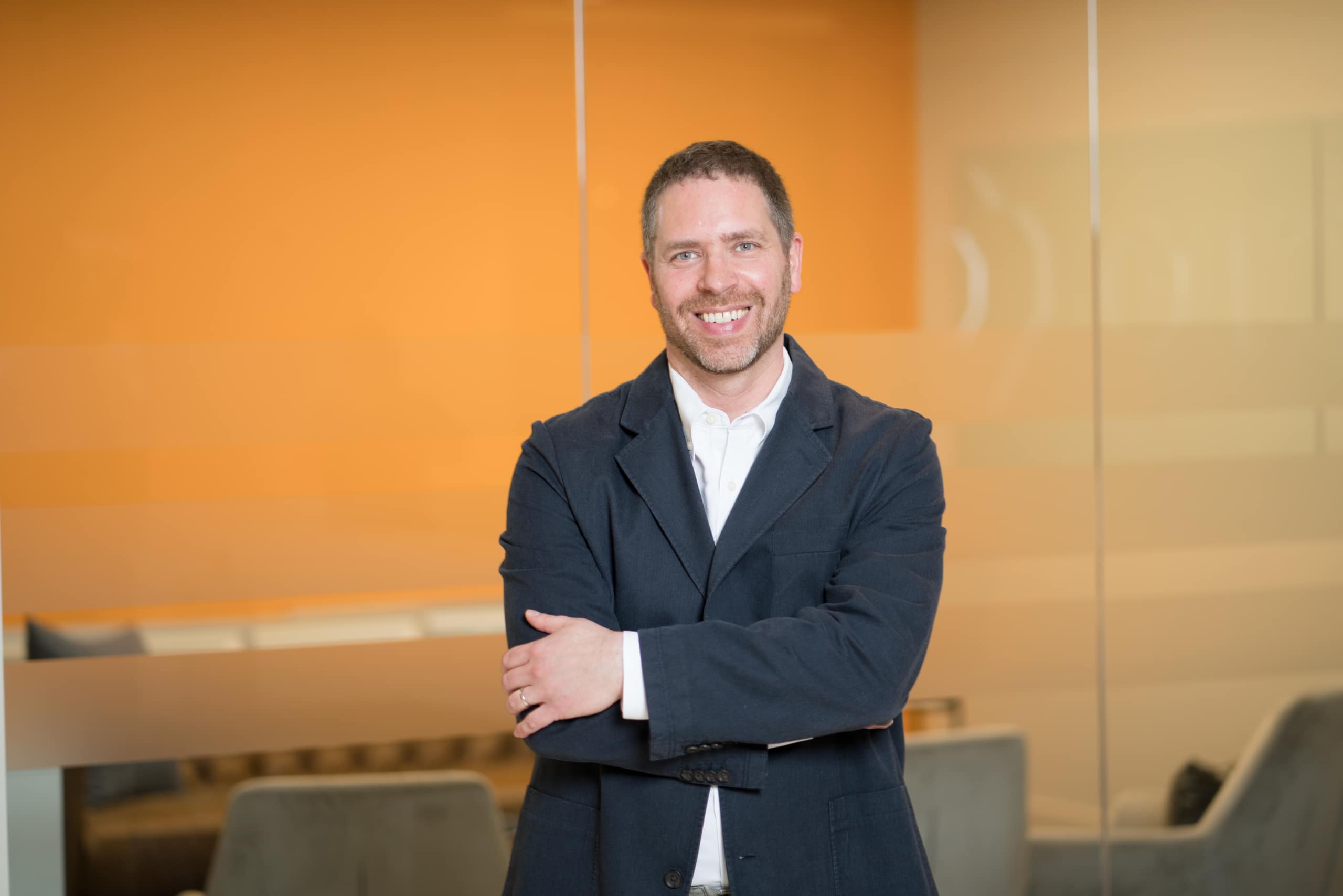 Man in suit jacket standing with his arms crossed in an Octo office