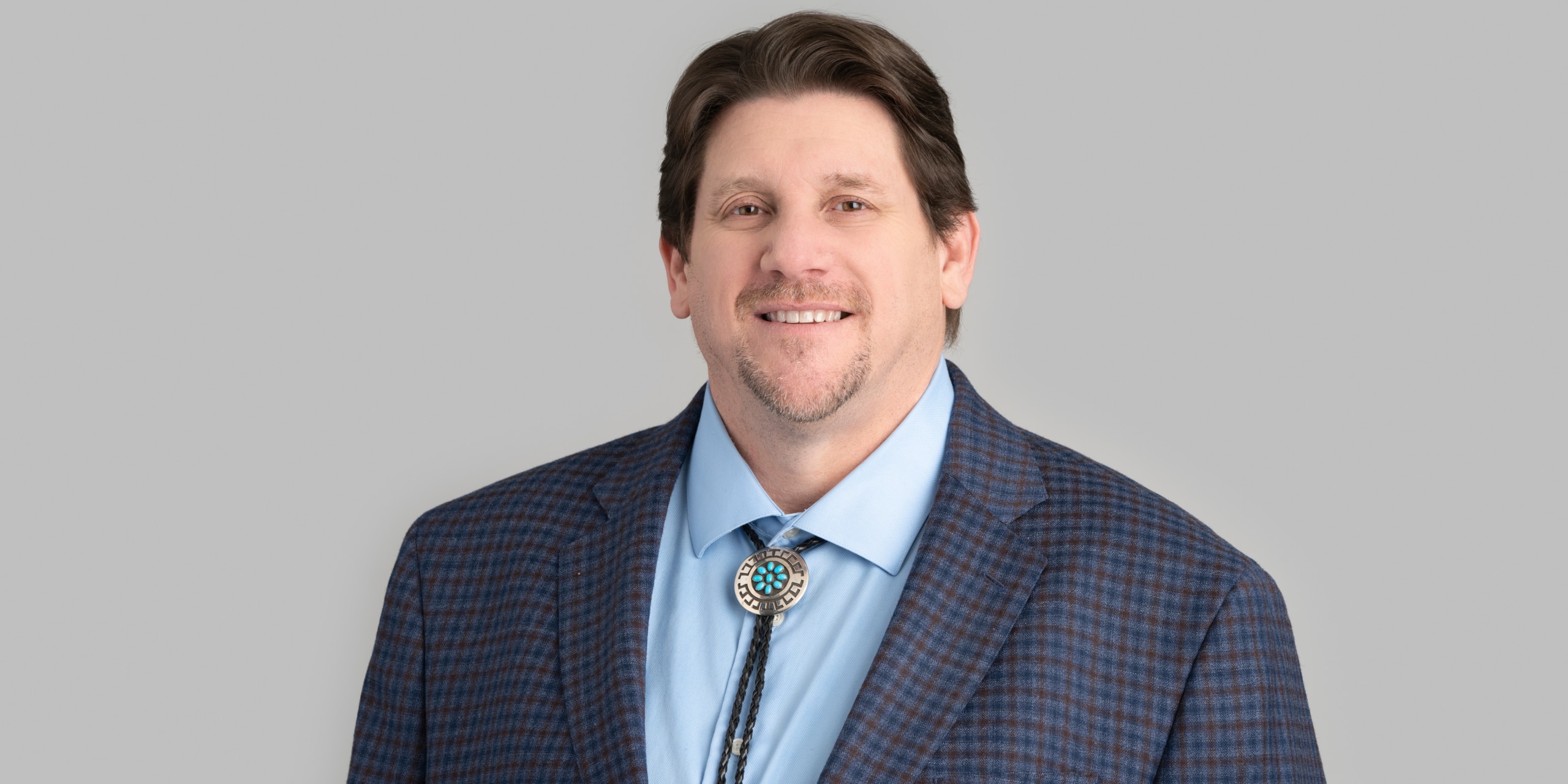 Man in suit jacket with blue collard shirt and bolo tie